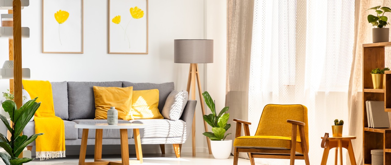  Bright, naturally lit living room featuring a grey sofa with yellow accent pillows, blankets, and accent chair.